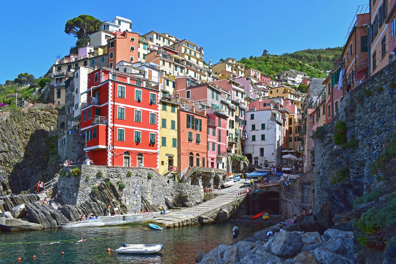 Blick vom Hafen auf Riomaggiore mit seinen bunten, mehrstöckigen Häusern an einem steilen Hang und kleinen Booten am Wasser.