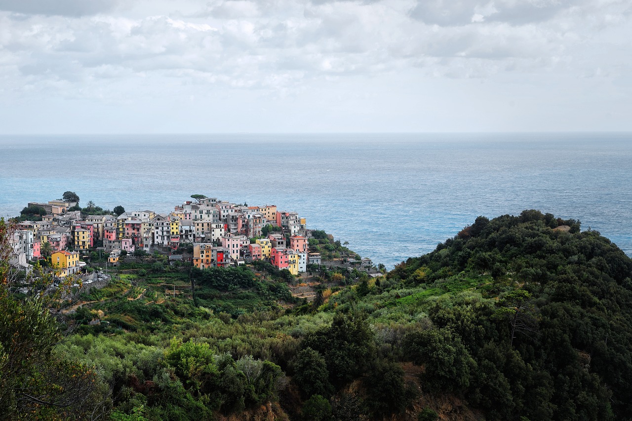 Das Dorf Corniglia auf einer Anhöhe über dem Meer mit bunten Häusern, engen Gassen und der Küste der Cinque Terre im Hintergrund.