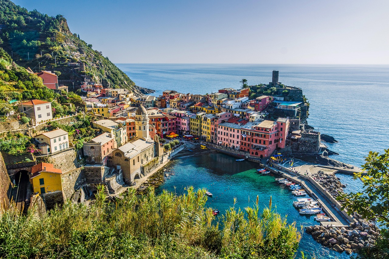 Blick von einem erhöhten Wanderweg auf das Küstendorf Vernazza mit bunten Häusern, kleinem Hafen und dem Ligurischen Meer im Hintergrund.
