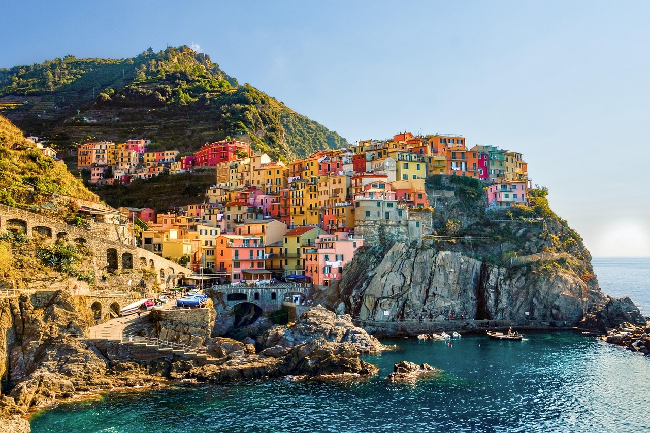 Blick vom Wasser auf das Küstendorf Manarola mit seinen bunten Häusern auf den Felsen und dem Ligurischen Meer im Vordergrund.