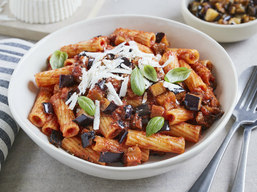 Eine servierte Portion Pasta alla Norma mit Nudeln, Auberginenstücken, Tomatensauce und geriebenem Käse auf einem Teller.