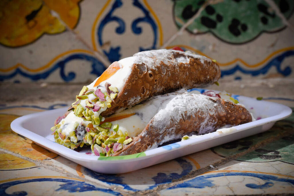 Knusprige Cannoli aus Teigrollen, gefüllt mit süßer Ricotta-Creme, teilweise mit Puderzucker und Pistazien garniert.