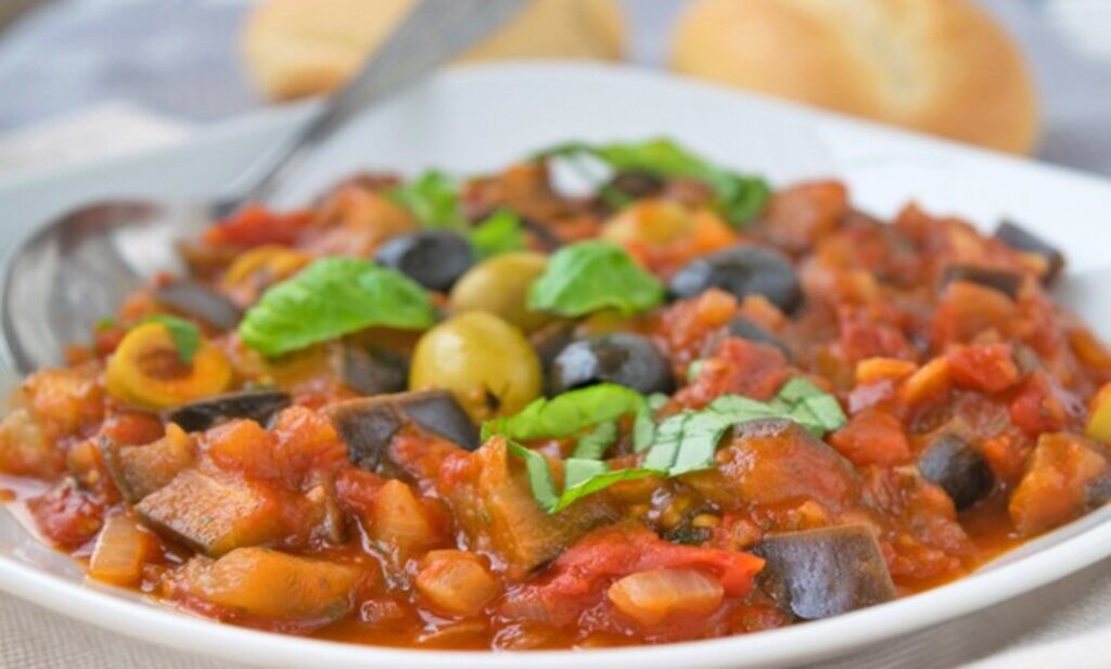 Ein Schüsselgericht mit Caponata aus Sizilien, bestehend aus gebratenen Auberginen, Tomaten, Sellerie, Oliven und Kapern in süß-saurer Sauce.