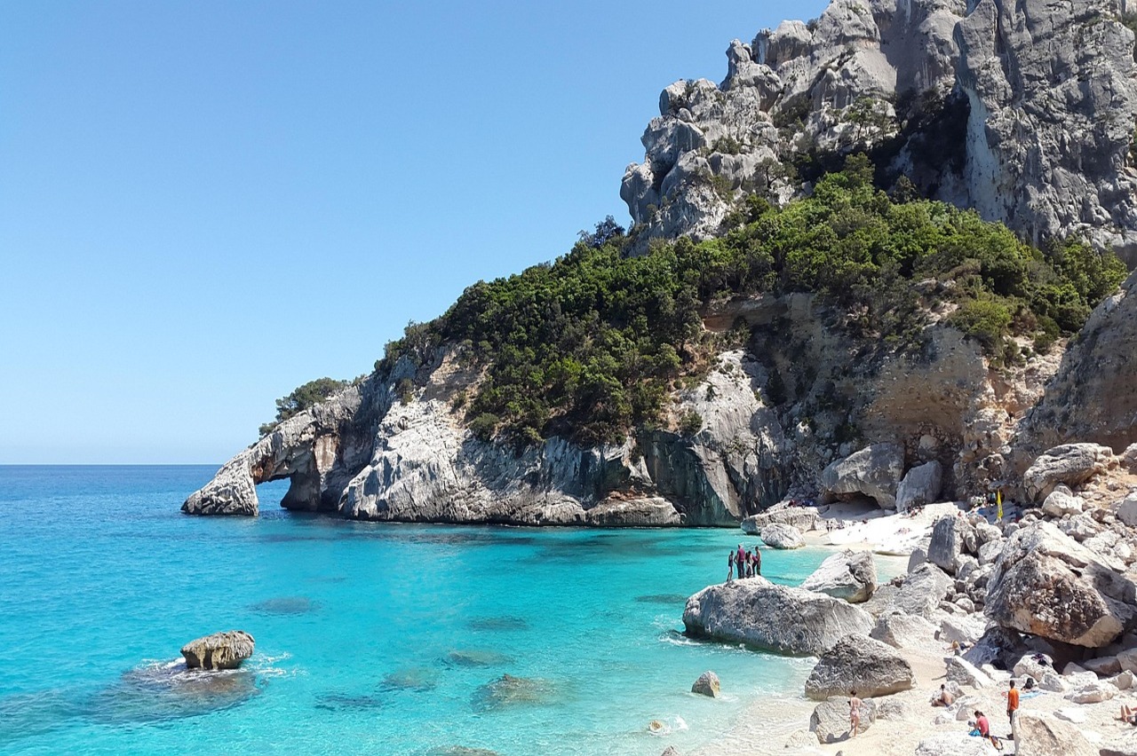 Cala Goloritzé auf Sardinien mit kristallklarem türkisblauem Wasser, weißem Kiesstrand und markanter Felsformation an der Küste Italiens
