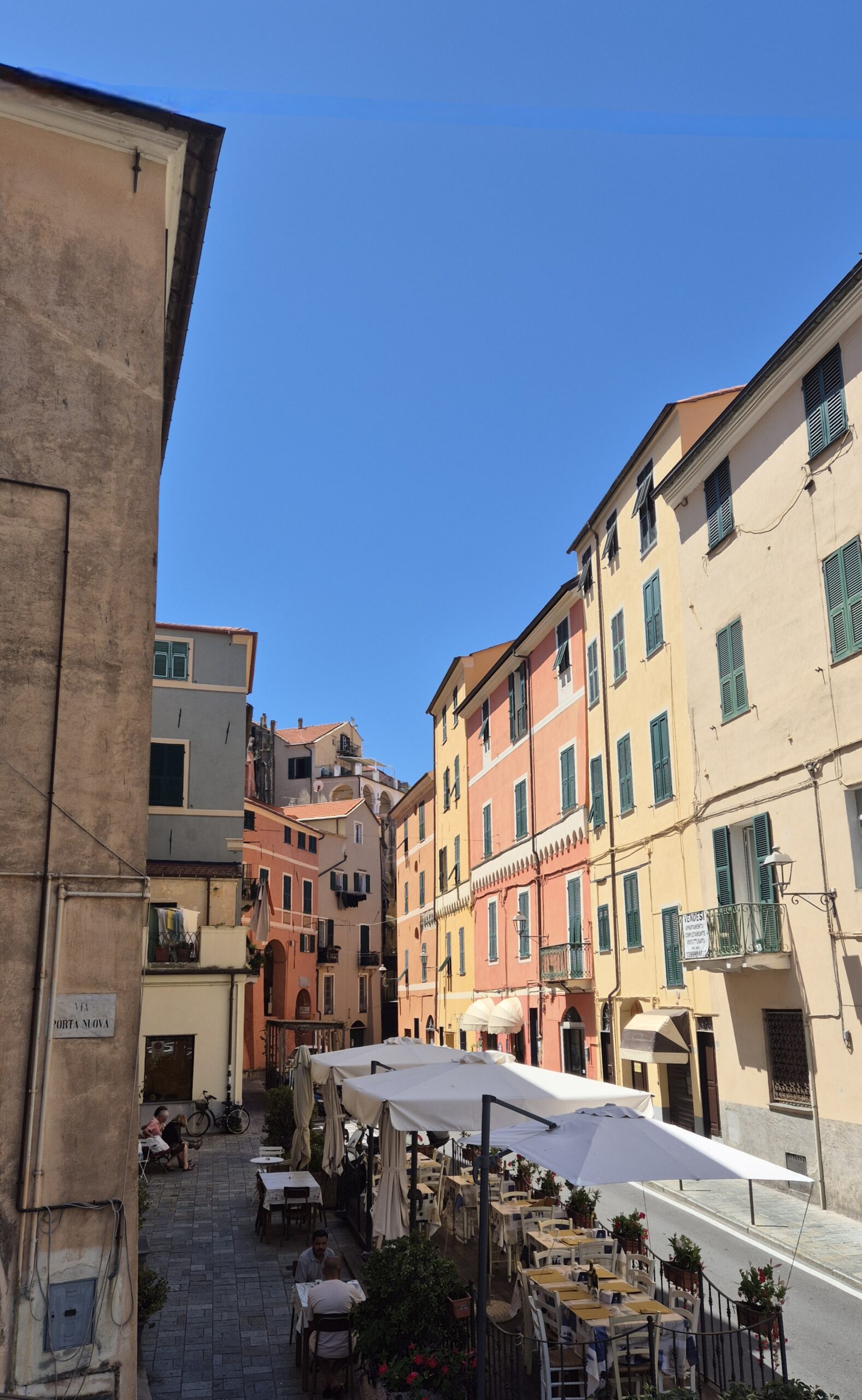 Bunte enge Gasse in Borgo Parasio in Imperia mit Restaurant, Gästen beim Essen im Freien und blauem Himmel in mediterraner Atmosphäre