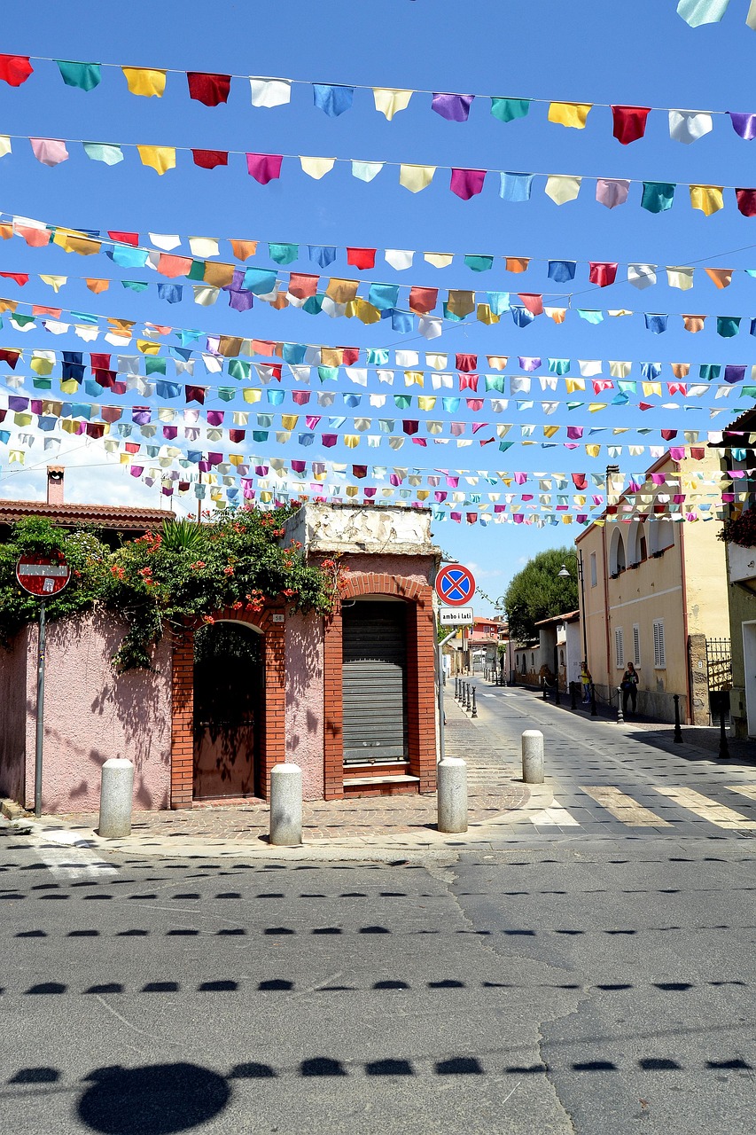 Altstadt von Pula auf Sardinien mit farbenfrohen Flaggen über der Straße, mediterraner Architektur und lebendiger Atmosphäre im historischen Ortskern