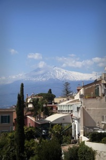 Panoramablick auf den verschneiten Ätna in Sizilien mit Häusern, mediterraner Vegetation und blauem Himmel im Hintergrund