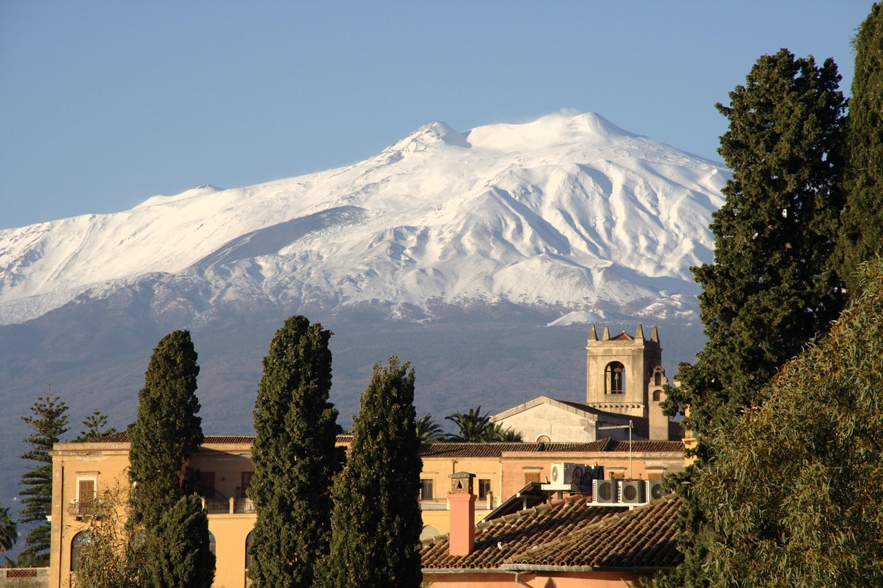 Blick auf den schneebedeckten Ätna über den Dächern Siziliens – beeindruckender Vulkan und beliebtes Ausflugsziel in Italien.