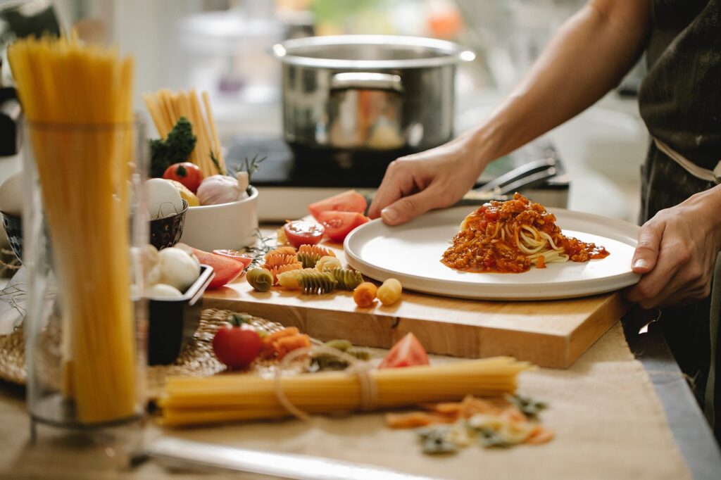 Frisch angerichtete Spaghetti mit Tomatensauce auf einem Teller, umgeben von Zutaten wie Pasta, Tomaten, Knoblauch und Kräutern in einer Küche.