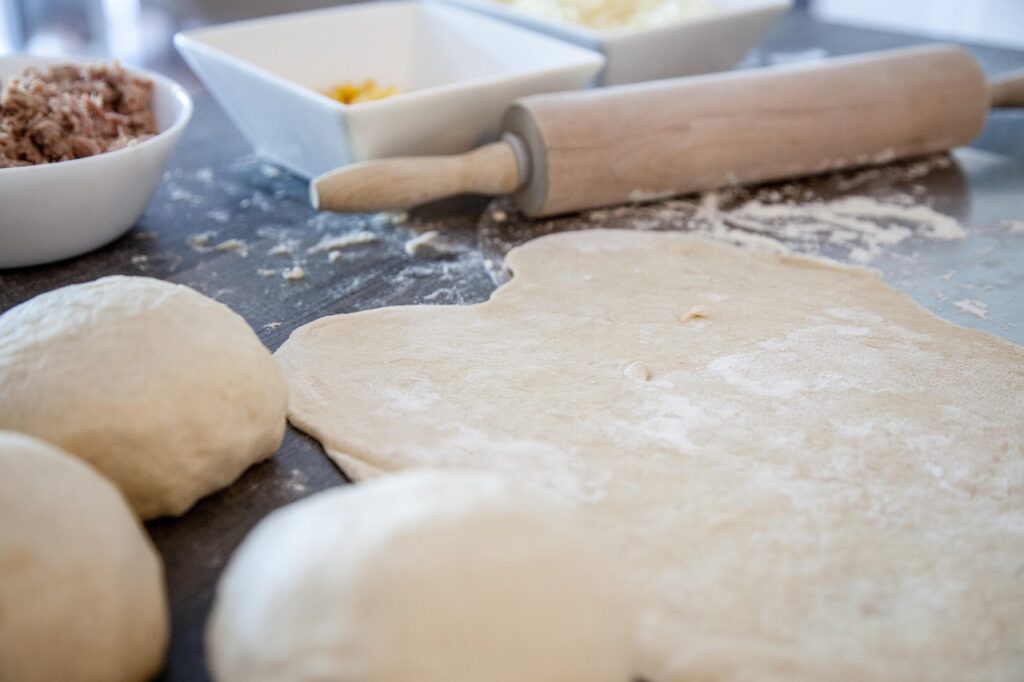 Frisch ausgerollter italienischer Pizzateig mit Teigkugeln, Mehl und Nudelholz auf einer Arbeitsfläche – Vorbereitung einer traditionellen Pizza.