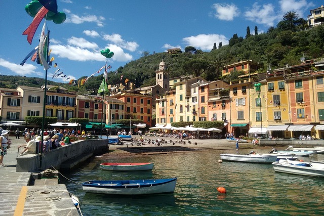 Blick auf den malerischen Hafen von Portofino mit bunten Häuserfassaden, kleinen Booten im Wasser und der Kirche San Giorgio auf dem Hügel.