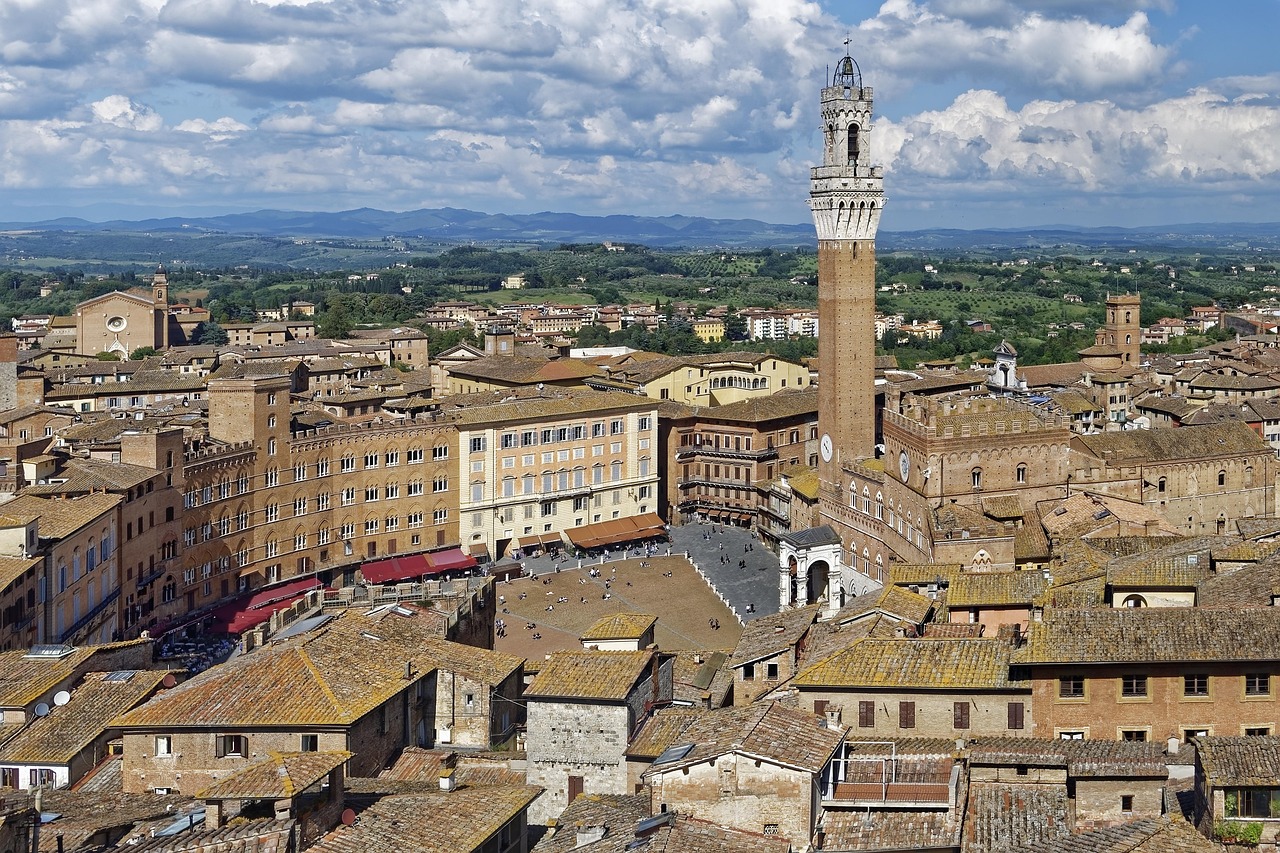 Panoramablick auf die Altstadt von Siena in der Toskana mit der Piazza del Campo, dem Torre del Mangia und historischen Gebäuden unter einem bewölkten Himmel.