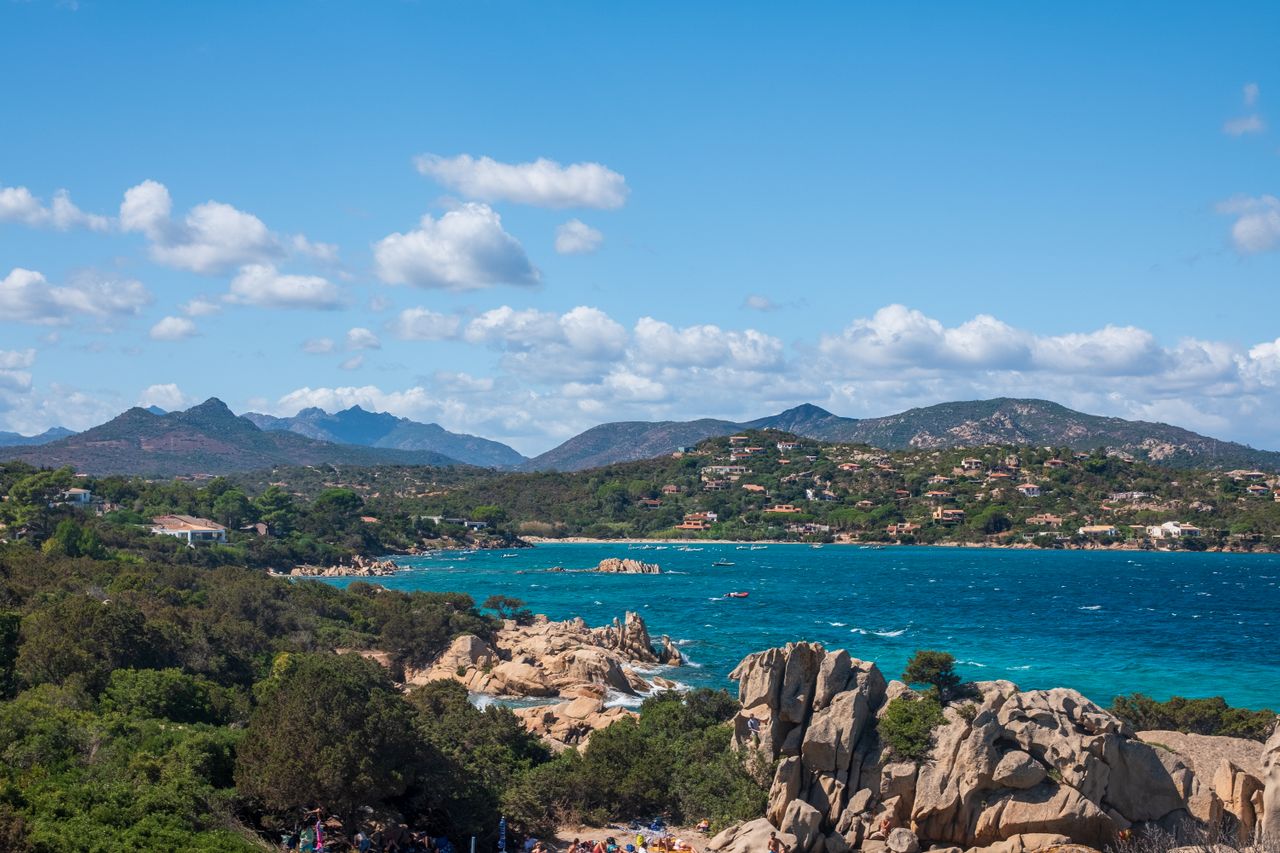 Cala Goloritzé auf Sardinien mit Strandbesuchern, türkisfarbenem klarem Wasser, Felsen und Bergen im Hintergrund